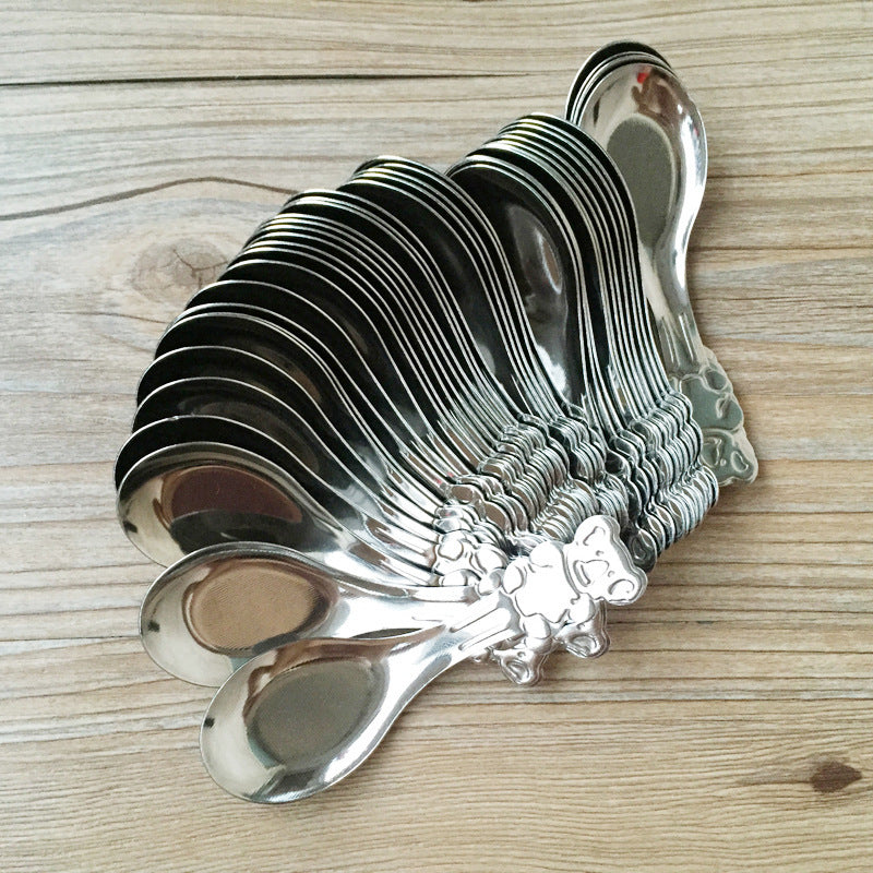 Set of silver spoons on a decorative holder with floral design on a wooden surface