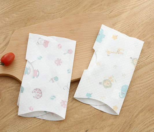 Two packs of patterned paper towels on a wooden surface with a cherry tomato.