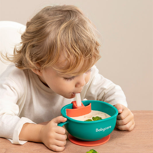 Child using a Babycare bowl with a spoon, sitting at a table.