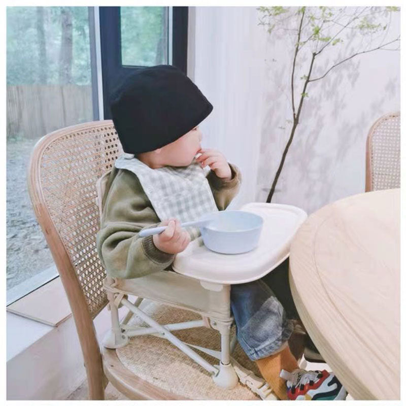 Child sitting at a table with a bowl, wearing a black beanie and green sweater.