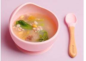 Pink bowl of soup with a spoon on a pink background