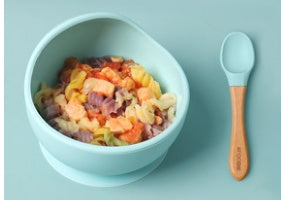 Bowl of colorful cereal with a wooden spoon on a light blue background