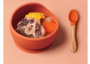 Orange bowl with soup and vegetables on a pink background