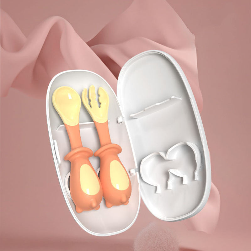 Set of orange baby spoons and fork in a white case on a pink fabric background