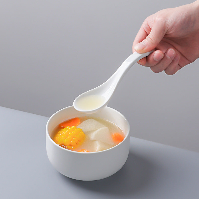 White bowl of soup with vegetables and a hand holding a white spoon against a gray background