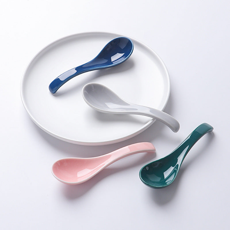 Four ceramic spoons in blue, white, pink, and green on a white plate against a white background.