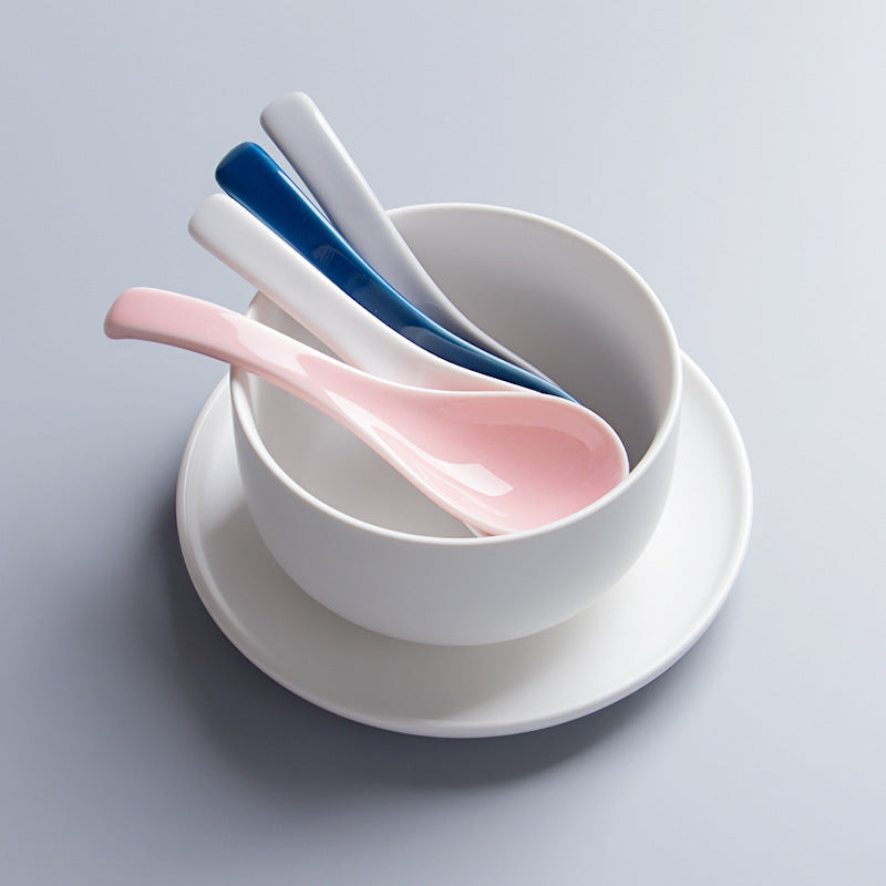 White bowl with pink and blue spoons on a light gray background