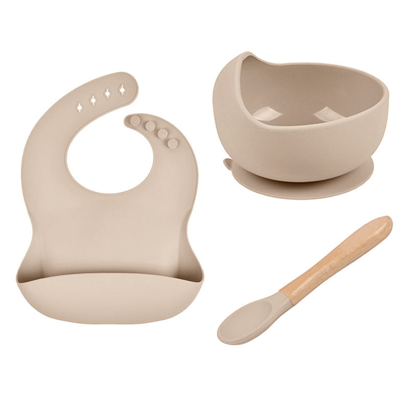 Beige baby bib, bowl, and spoon set on a white background