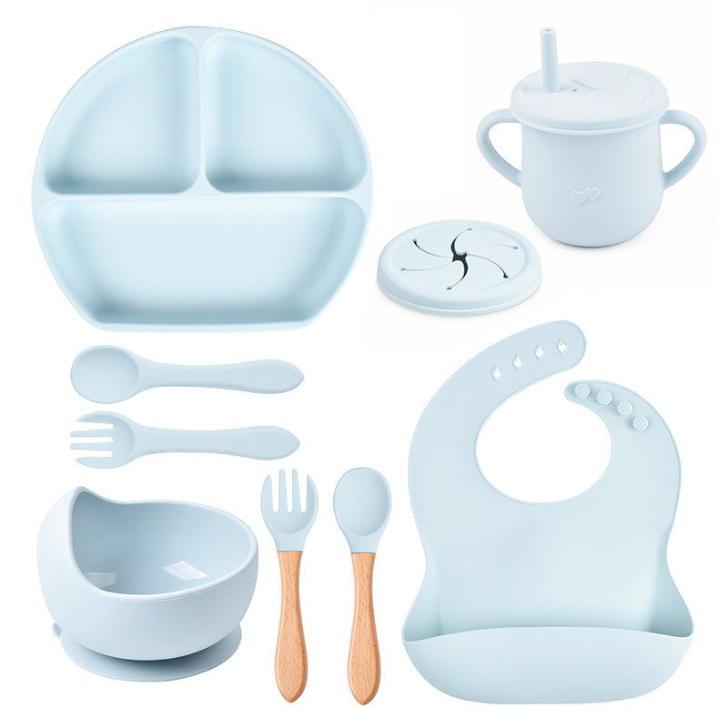 Set of baby dining utensils including a plate, cup, bowl, spoon, fork, and bib in light blue color on a white background.