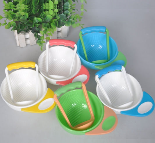Colorful children's sand toys including buckets and shovels on a gray surface with a plant in the background.