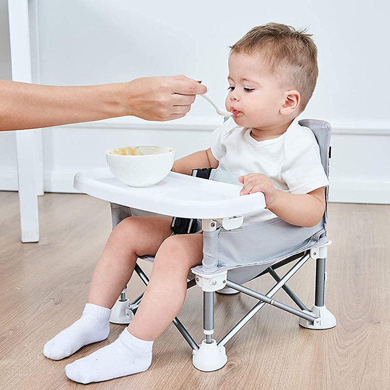 Child sitting in a portable folding chair being fed by an adult.