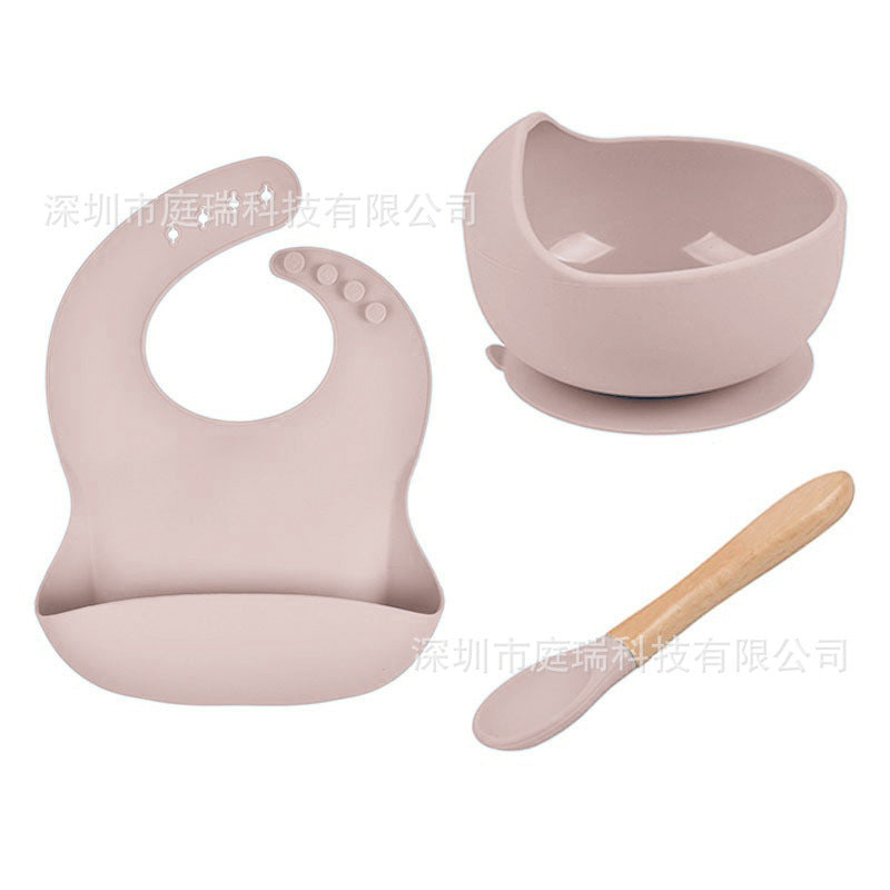 Pink baby bib, bowl, and wooden spoon set on a white background