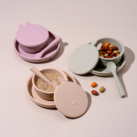 Set of children's silicone bowls and spoons on a light pink background