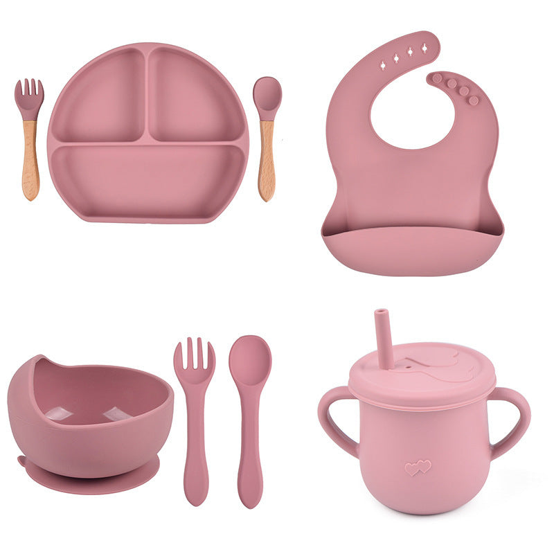 Pink children's dining set including plate, bowl, cup, utensils, and bib on a white background