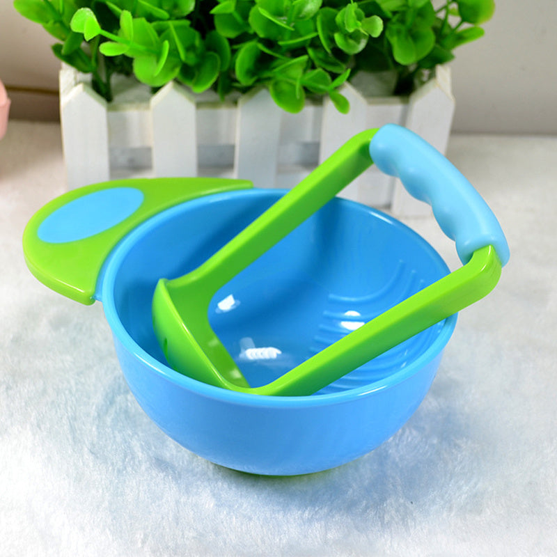 Blue bowl with green handles on a white surface, with a plant in the background.