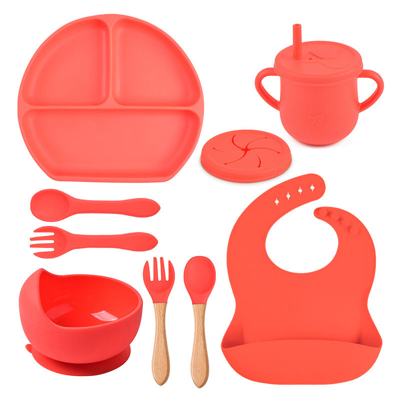 Red silicone dining set including plate, cup, bowl, utensils, and bib on a white background