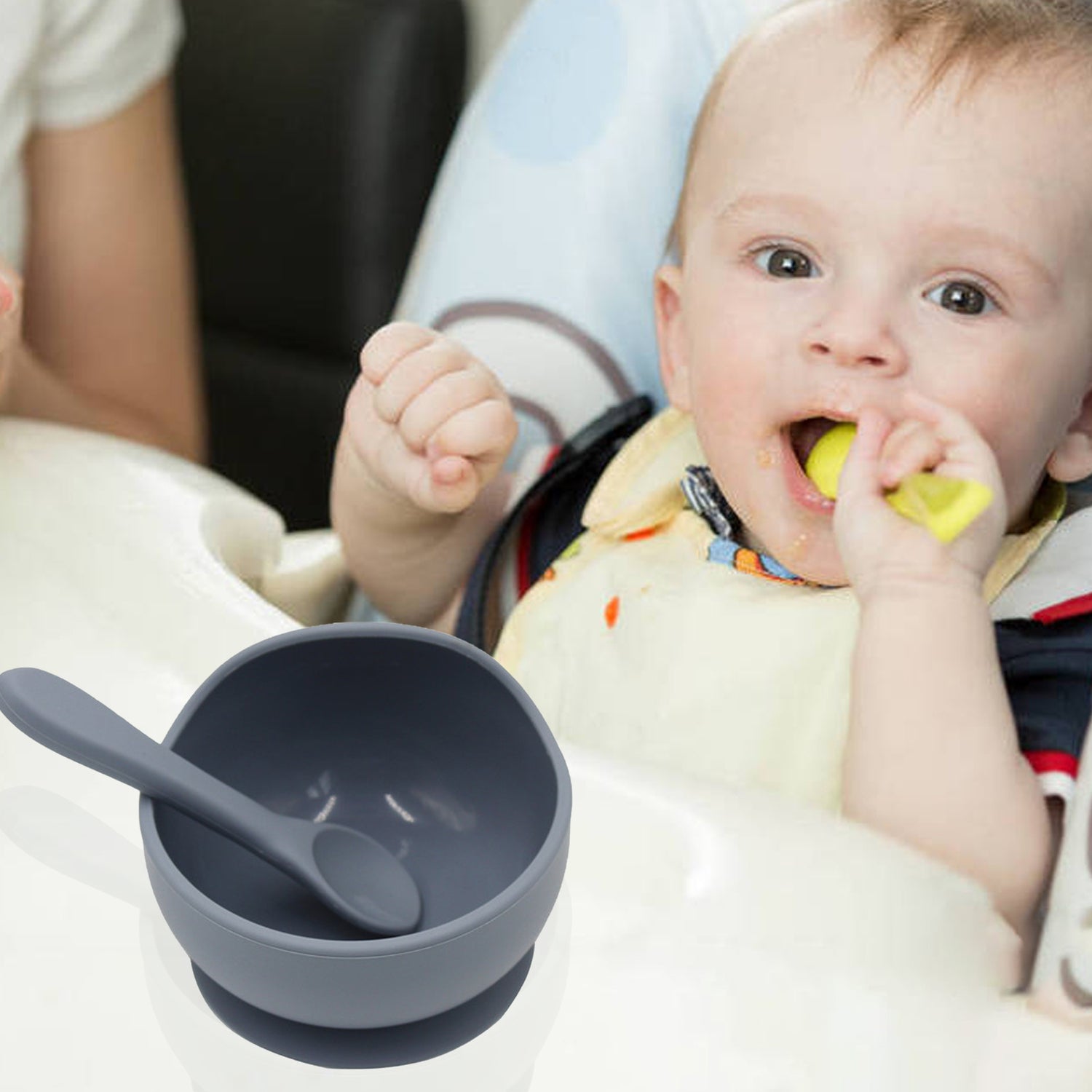Baby sitting in a high chair with a gray bowl and spoon, holding a yellow object.