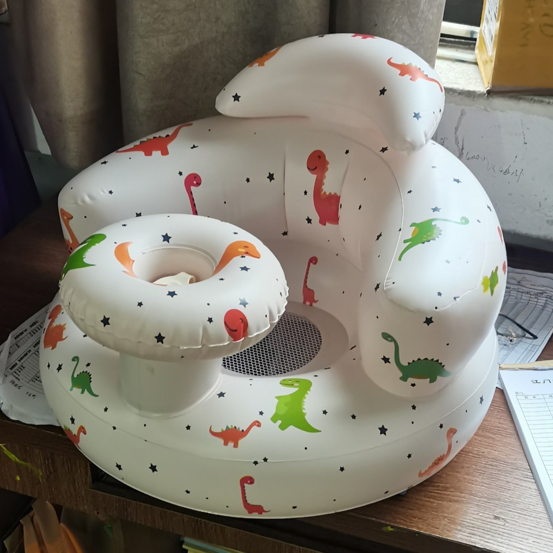 Baby seat with dinosaur patterns on a wooden surface