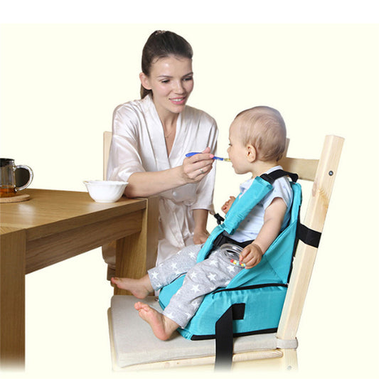 Woman feeding a child in a blue booster seat at a dining table.