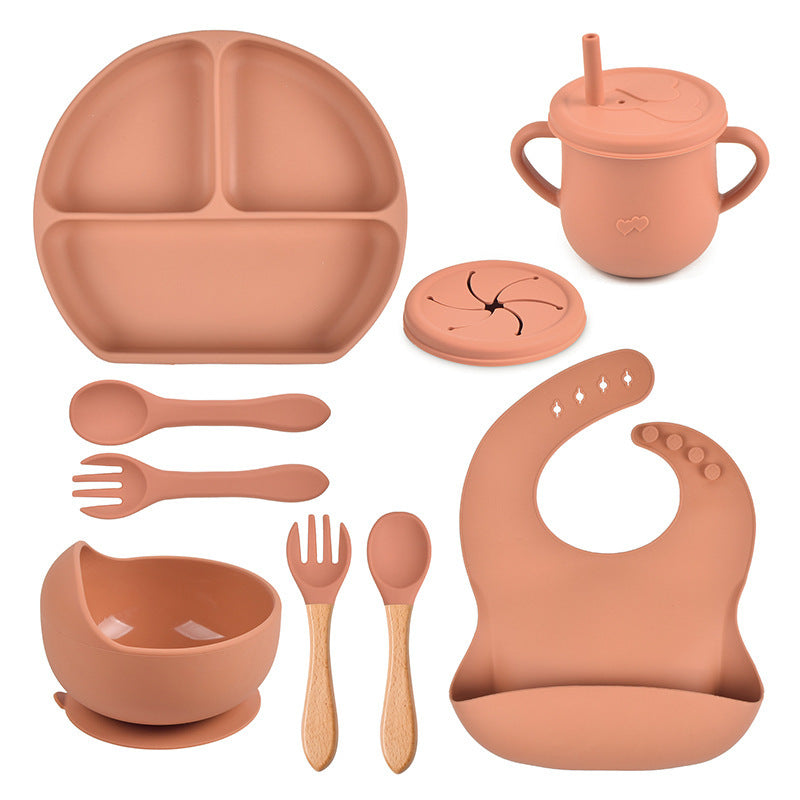 Terracotta-colored children's dining set including plate, cup, bowl, utensils, and bib on a white background.