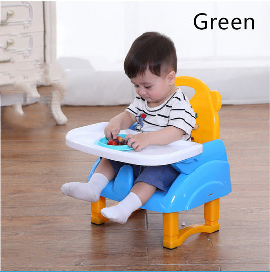 Child sitting in a blue and yellow booster seat with a plate of food on a wooden floor.