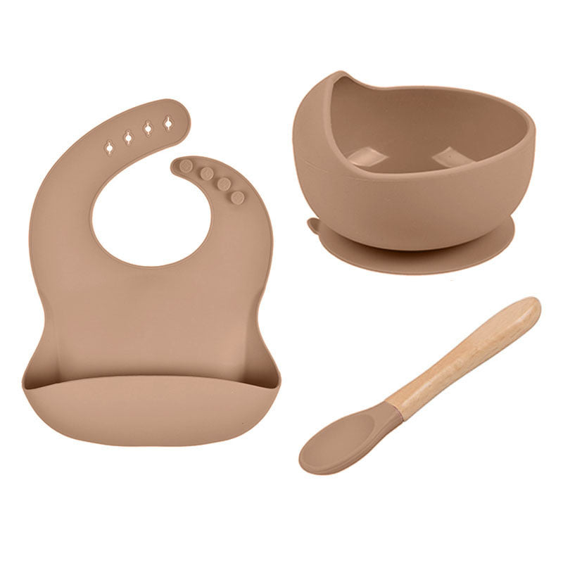 Set of baby feeding utensils including a bib, bowl, and spoon in a beige color on a white background.