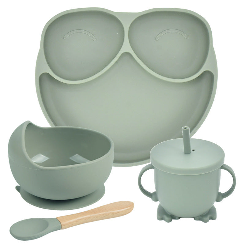 Set of green silicone dining utensils including a tray, bowl, cup with straw, and spoon on a white background.