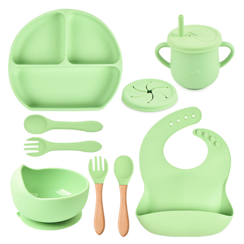 Green silicone dining set including plate, cup, bowl, utensils, and bib on a white background