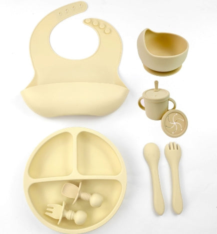 Beige baby dining set including bib, plate, cup, and utensils on a white background