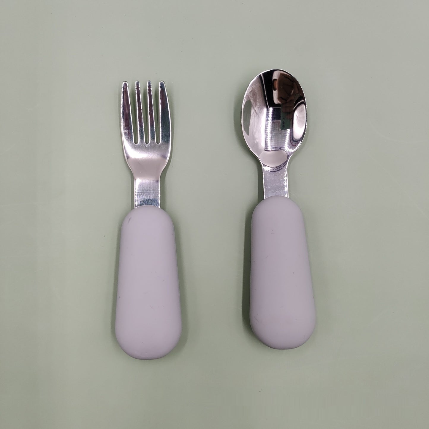 Silver fork and spoon with purple handles on a light green background