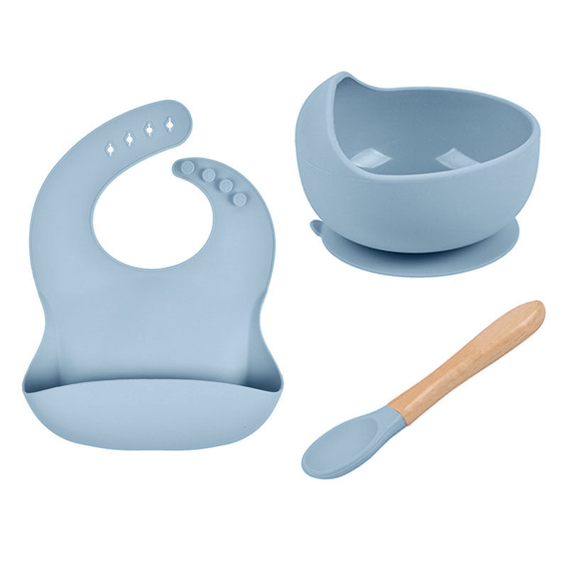 Blue baby bib, bowl with suction cup, and wooden spoon on a white background