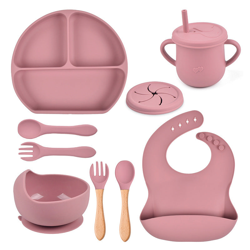 Pink children's dining set including plate, cup, utensils, and bib on a white background