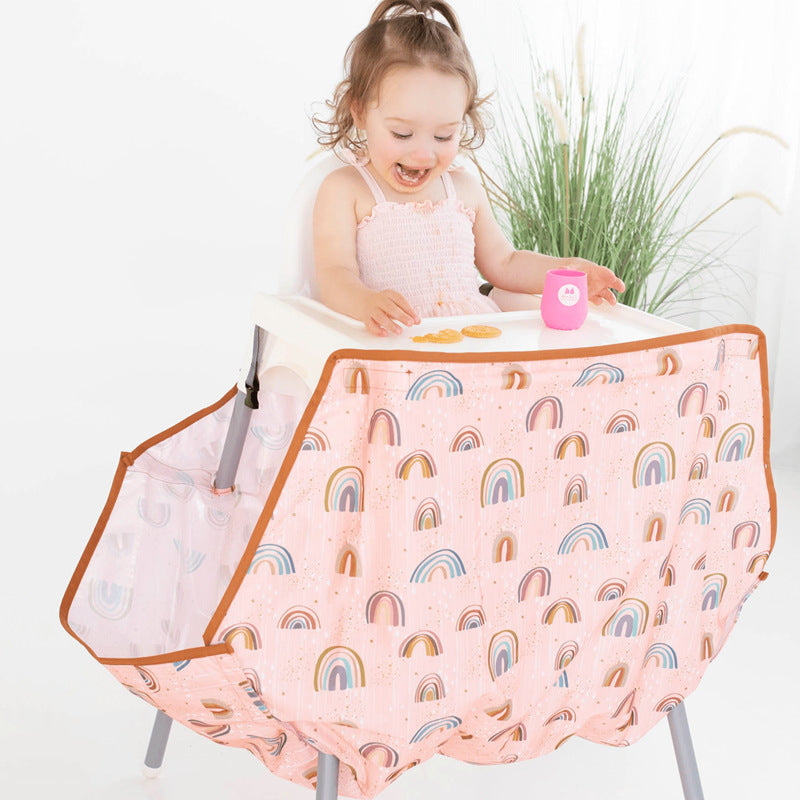 Child playing with a pink high chair cover with rainbow pattern on a white background