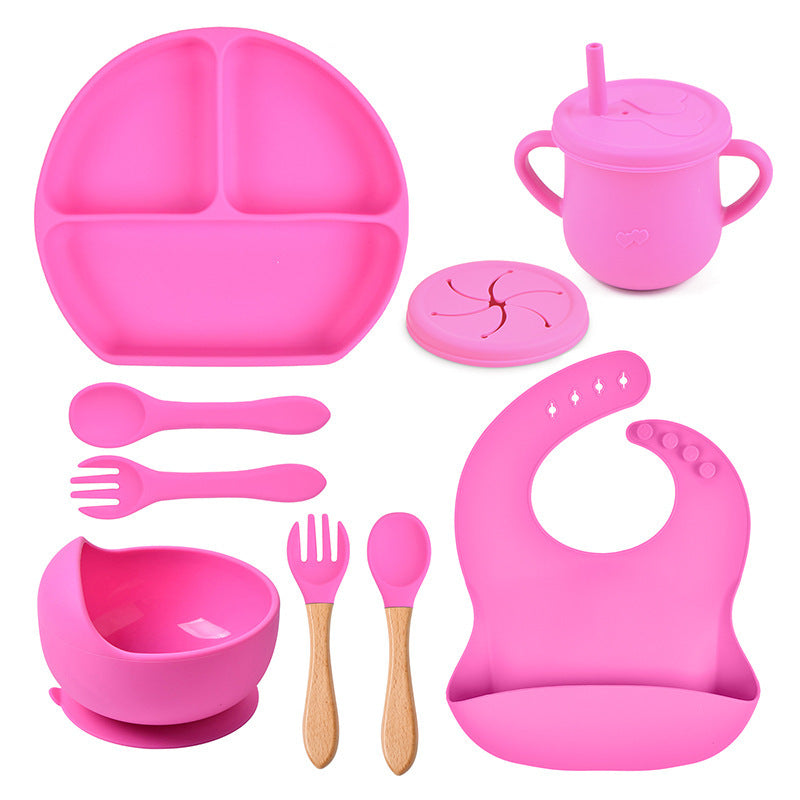 Pink children's dining set including plate, cup, bowl, utensils, and bib on a white background