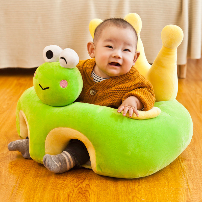 Child sitting on a green caterpillar-shaped cushion on a wooden floor.