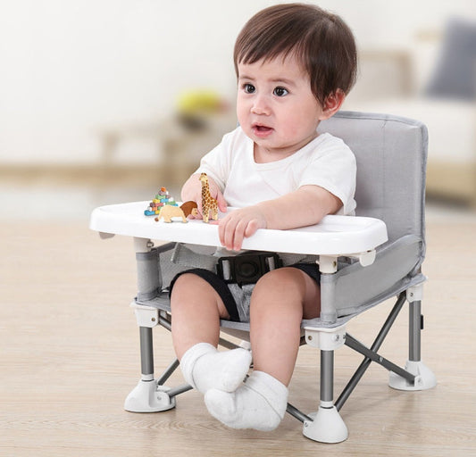 Child sitting in a portable high chair with a white tray and gray frame.