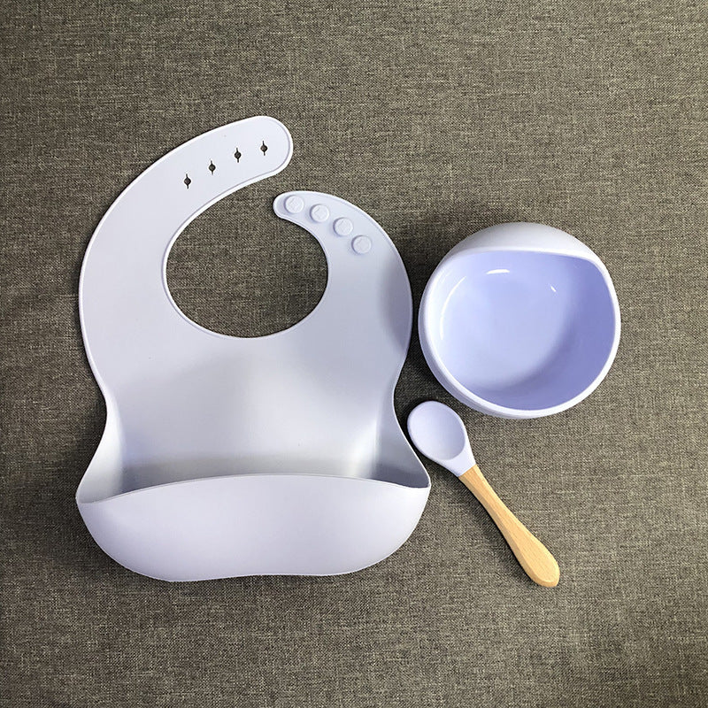 White silicone bib, bowl, and spoon on a brown textured surface