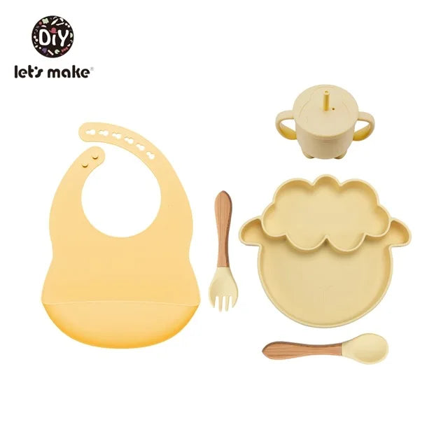 Baby dining set with bib, plate, cup, fork, and spoon on a white background.