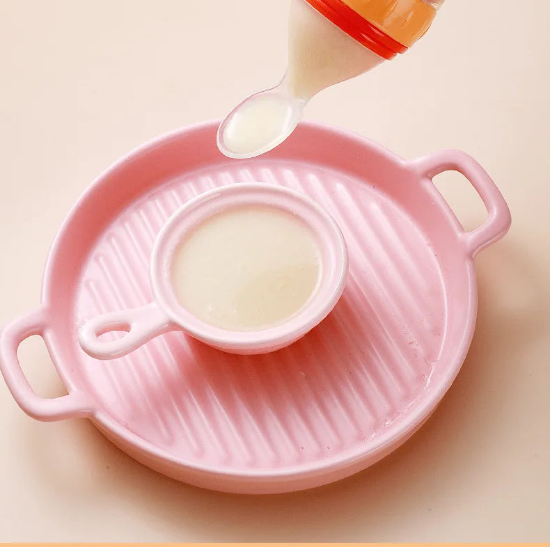 Pink baby bottle with a spoon pouring milk into it on a beige background