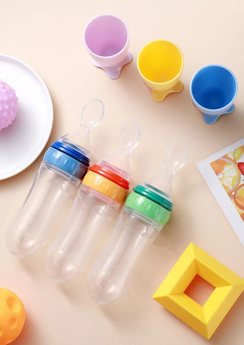 Colorful baby bottles with caps on a light surface with toys around