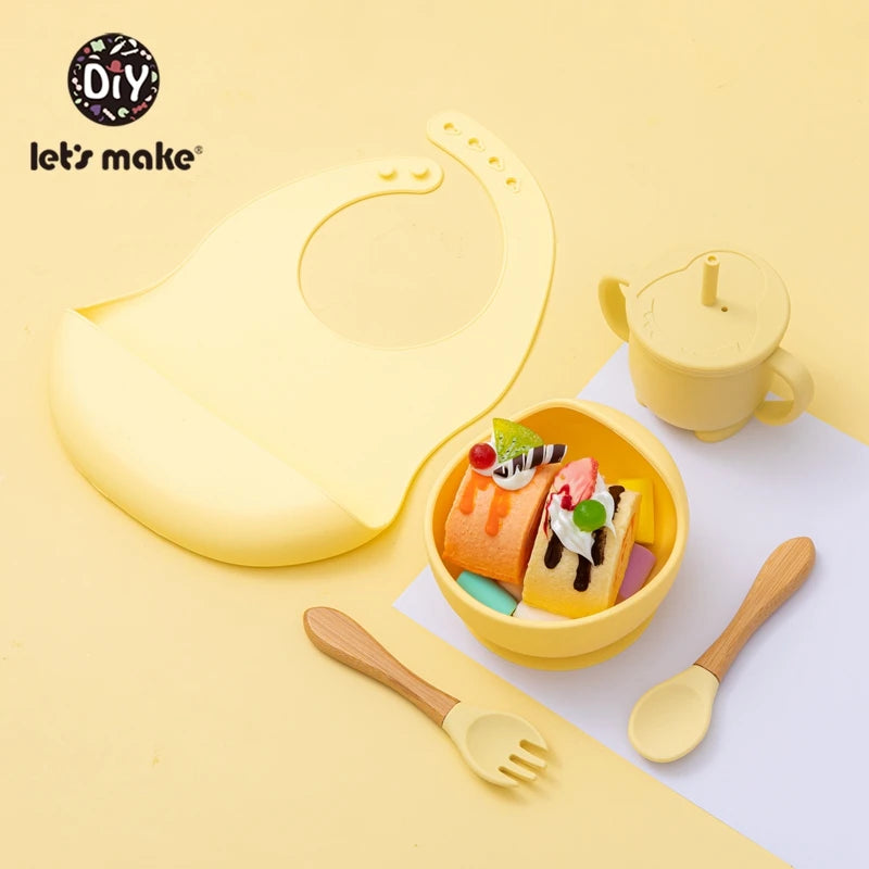 Yellow children's tableware set including a bowl, cup, spoon, and fork on a yellow background with 'let's make' branding.