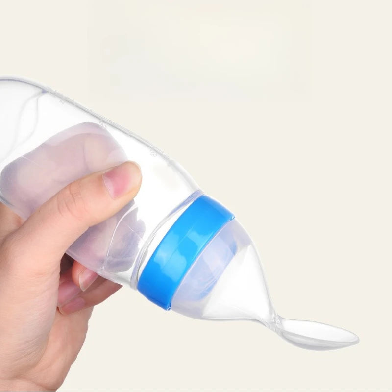 Hand holding a clear baby bottle with a blue cap on a light background