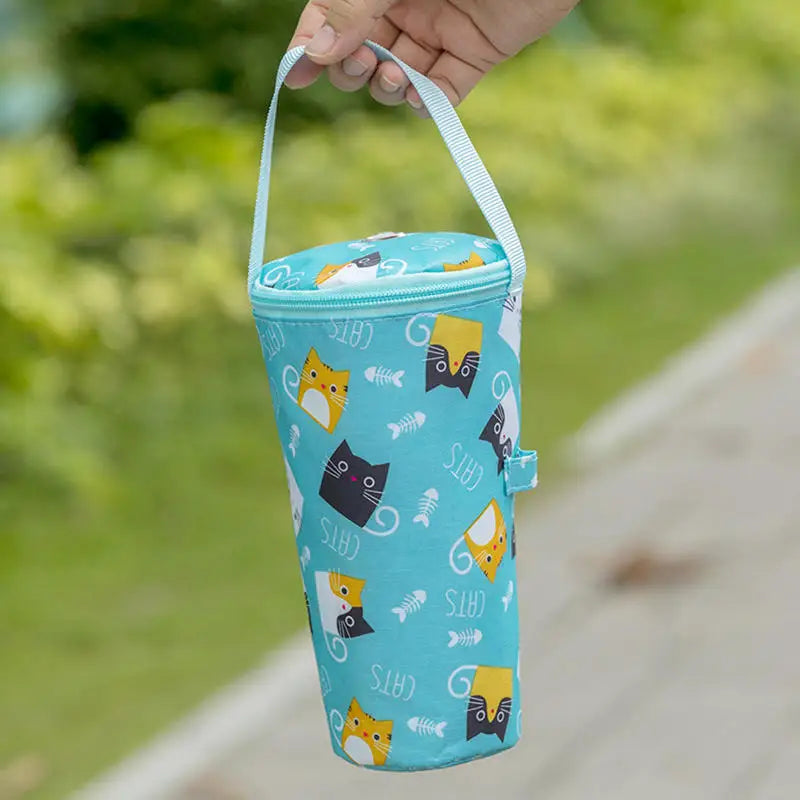 Blue cylindrical bag with cat pattern held by a hand outdoors