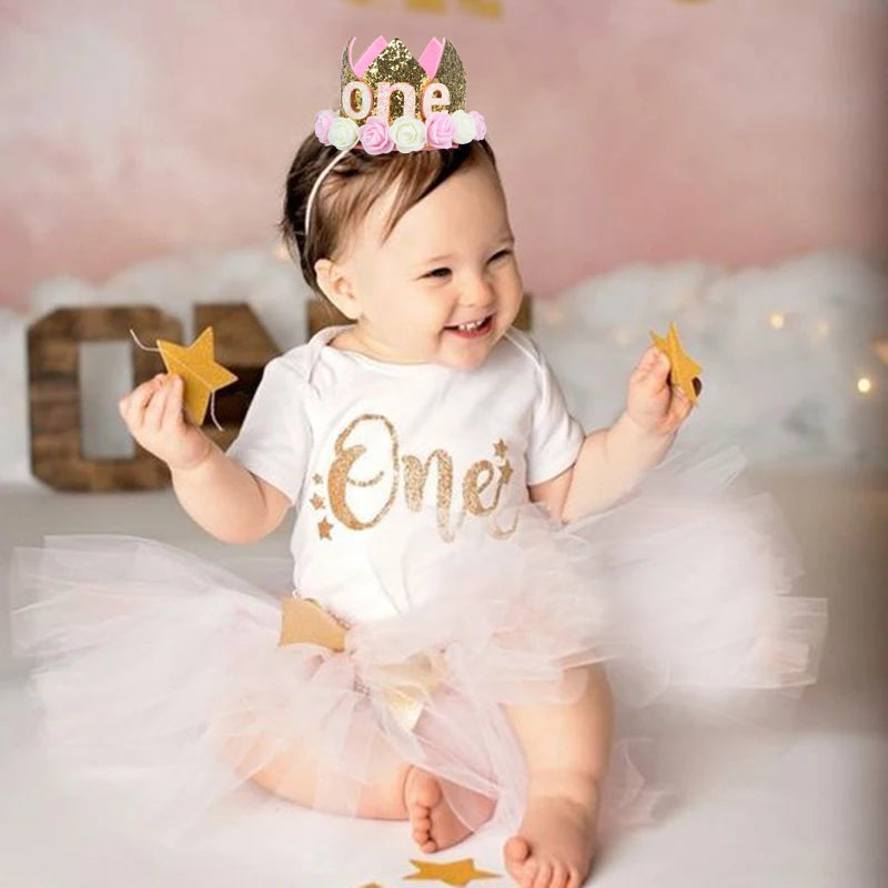 Baby in a 'One' outfit with a tutu and floral crown, celebrating a first birthday.