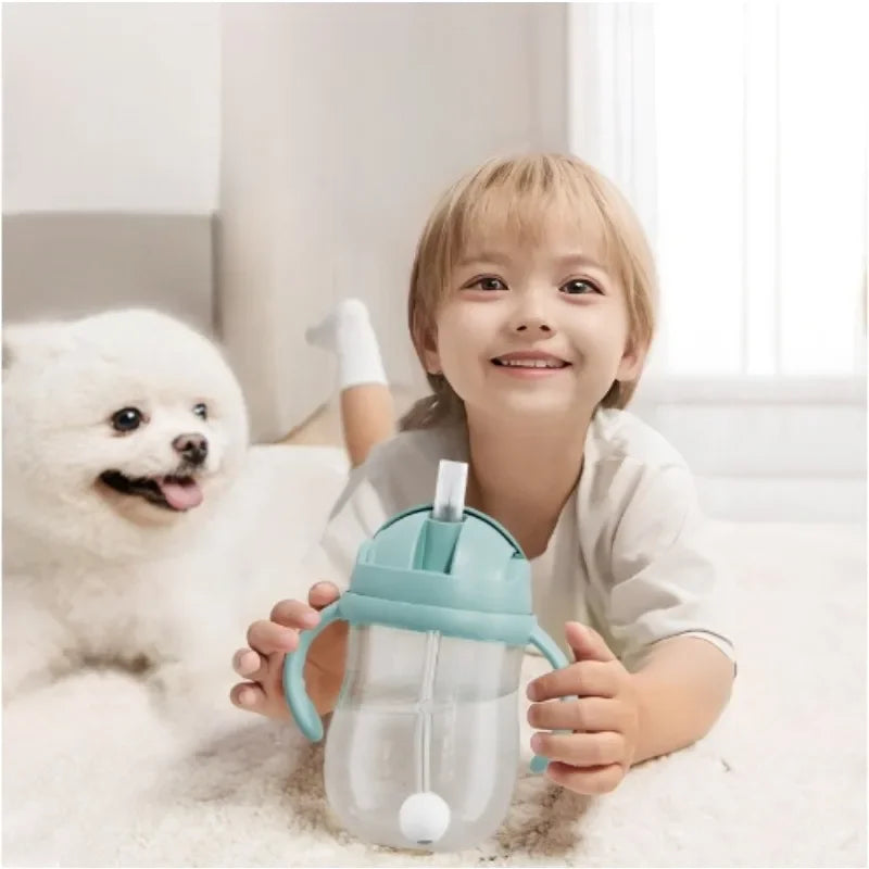 Child holding a blue sippy cup with a white dog sitting next to them on a light-colored couch.