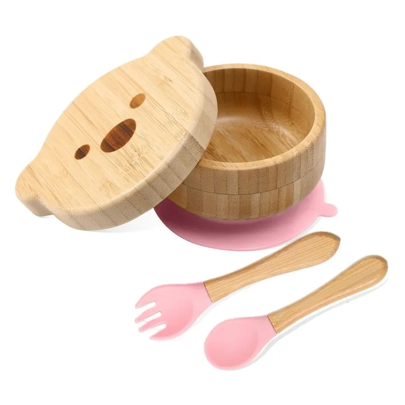 Bamboo baby bowl with lid, pink suction cup, fork, and spoon set on a white background