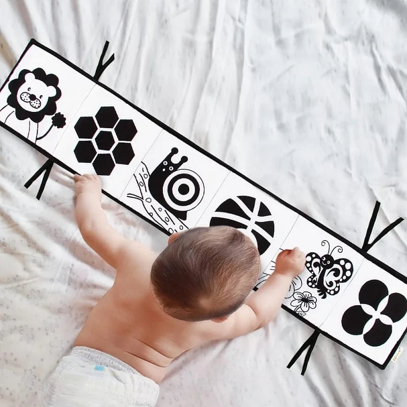 Baby playing with a black and white patterned board on a white blanket