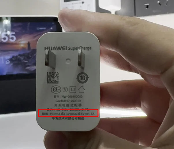Hand holding a Huawei SuperCharge wall adapter with visible specifications.