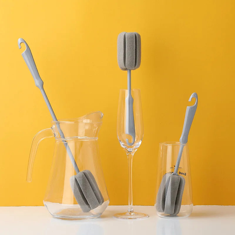 Three gray silicone bar brushes in use with a pitcher, glass, and wine glass on a yellow background.