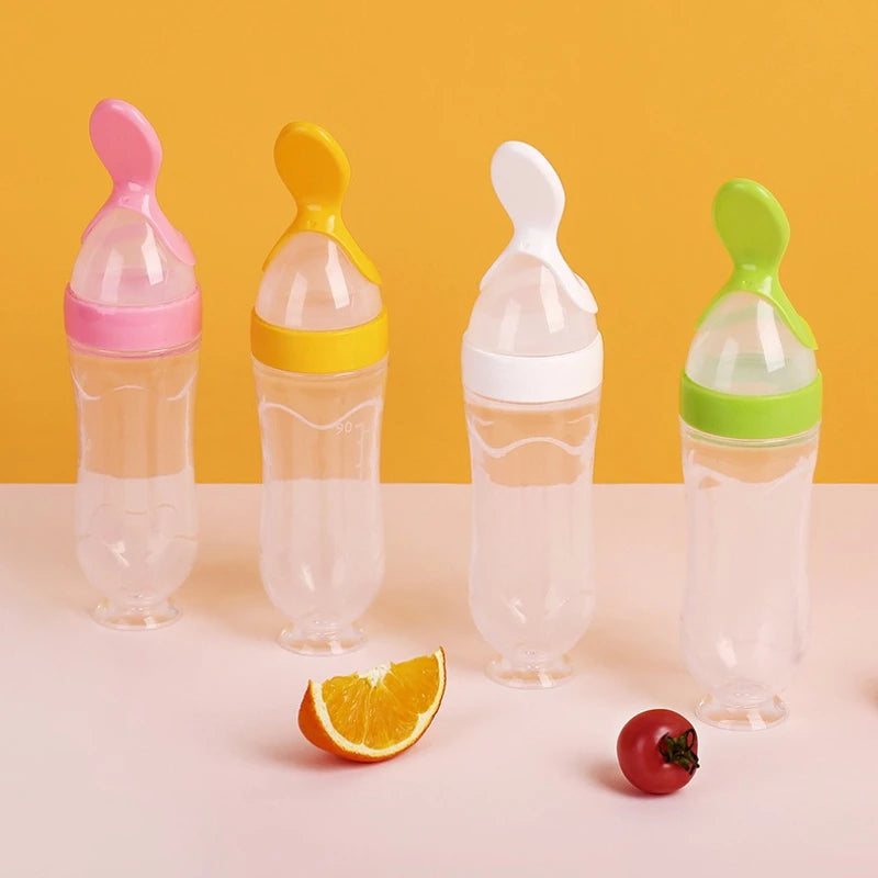 Silicone baby feeding bottles with squeeze spoons in green, yellow, pink, and clear by Nestacular.